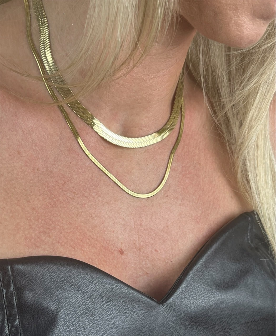 Nærbillede af bred guldbelagt snake-halskæde med glat, skinnende overflade – et tidløst statement-piece, der tilføjer elegance til enhver stil.