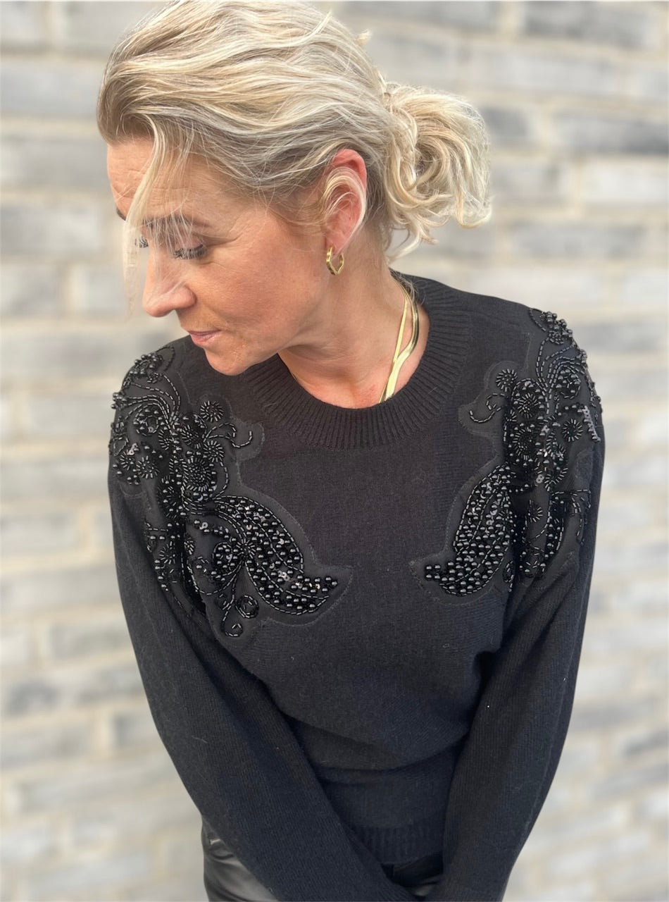 Nærbillede af den bløde, sorte strik med skinnende sorte perler og pailletter – elegant, underspillet og lidt ekstra.