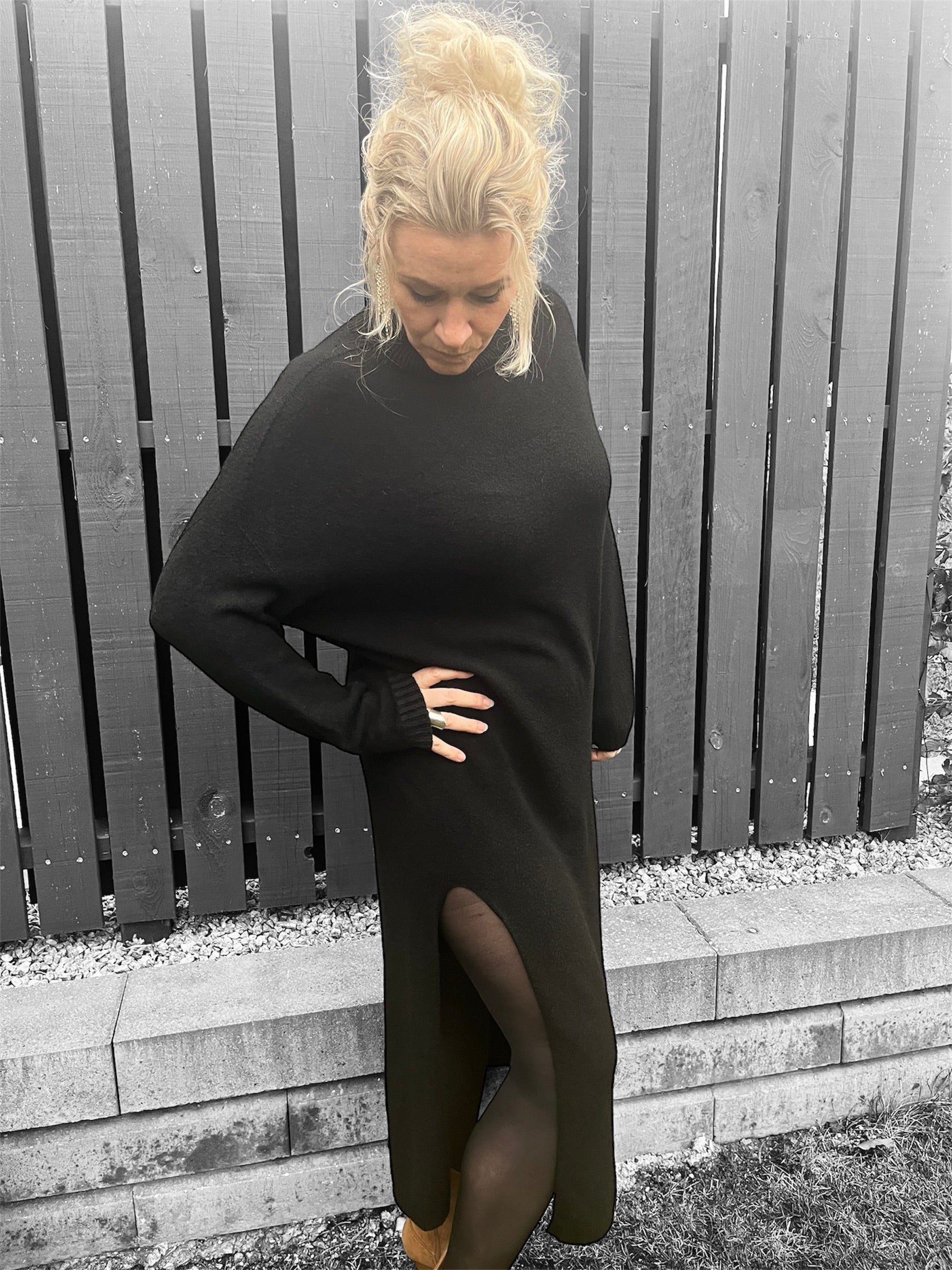 Model iført sort strikkjole med høj hals og sideslids, stående mod en neutral baggrund.