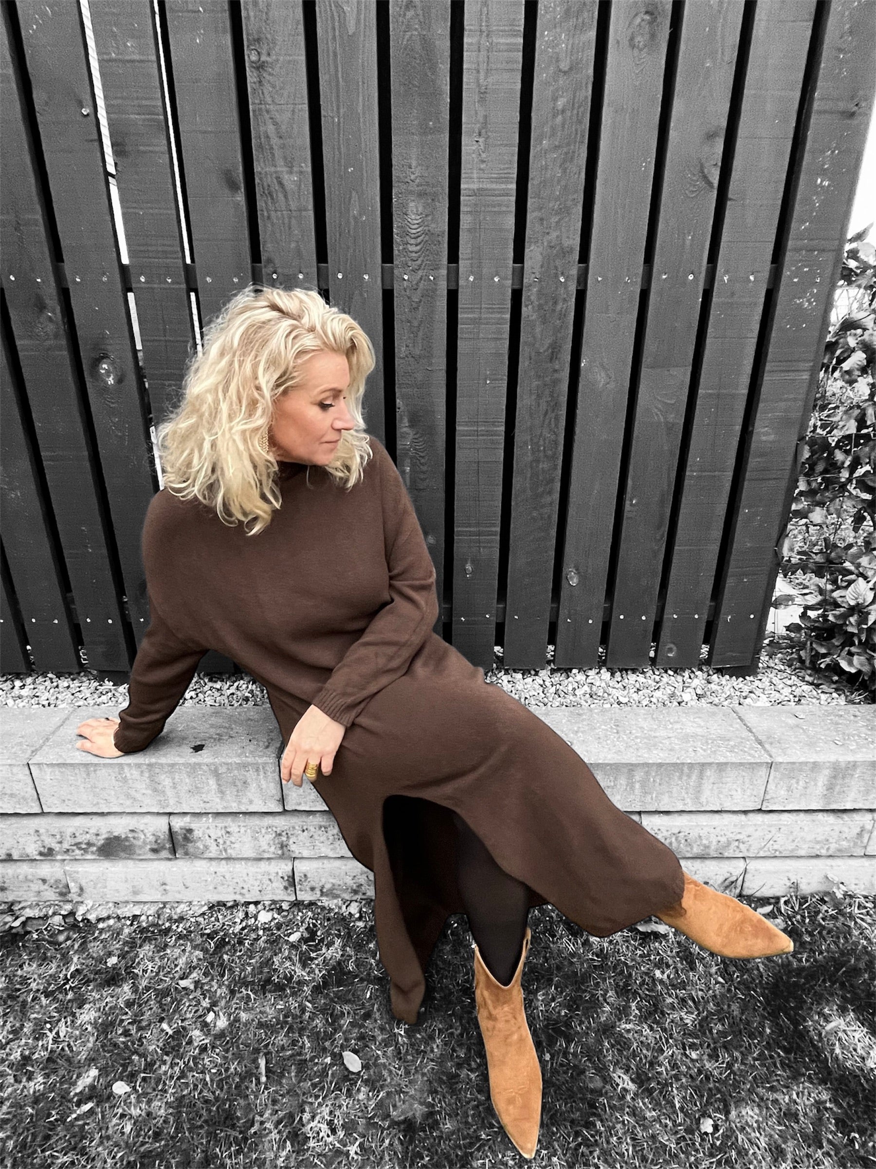 Model i brun kjole fotograferet siddene og med fokus på kjolens slids og bløde fald.