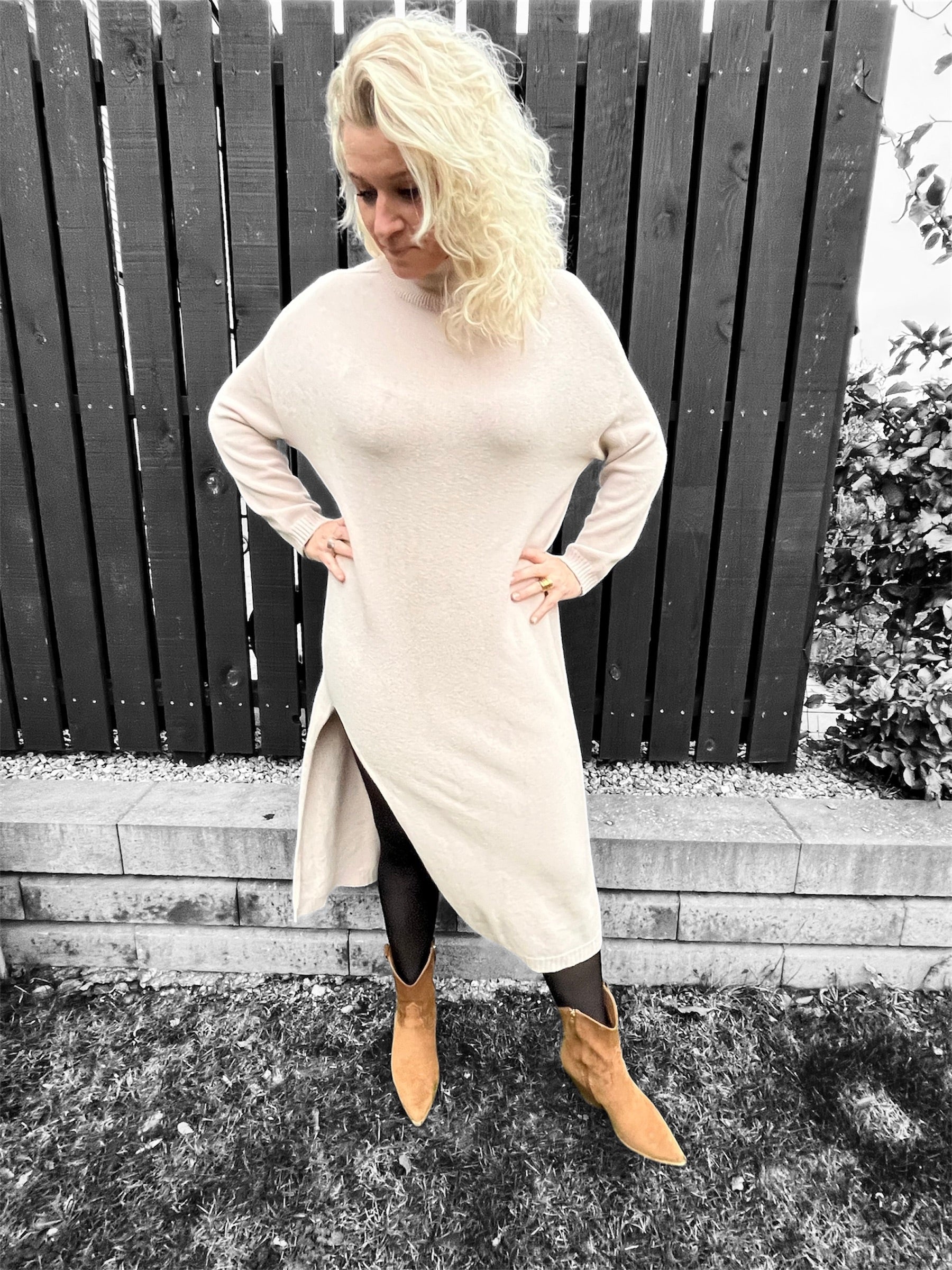 ​Model iført beige strikkjole med høj hals og sideslids, stående mod en neutral baggrund.