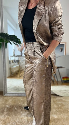 Model iført champagnefarvede Bydalona Pants fra SpohrCopenhagen med skinnende finish og brede ben – klar til at danse natten væk."
