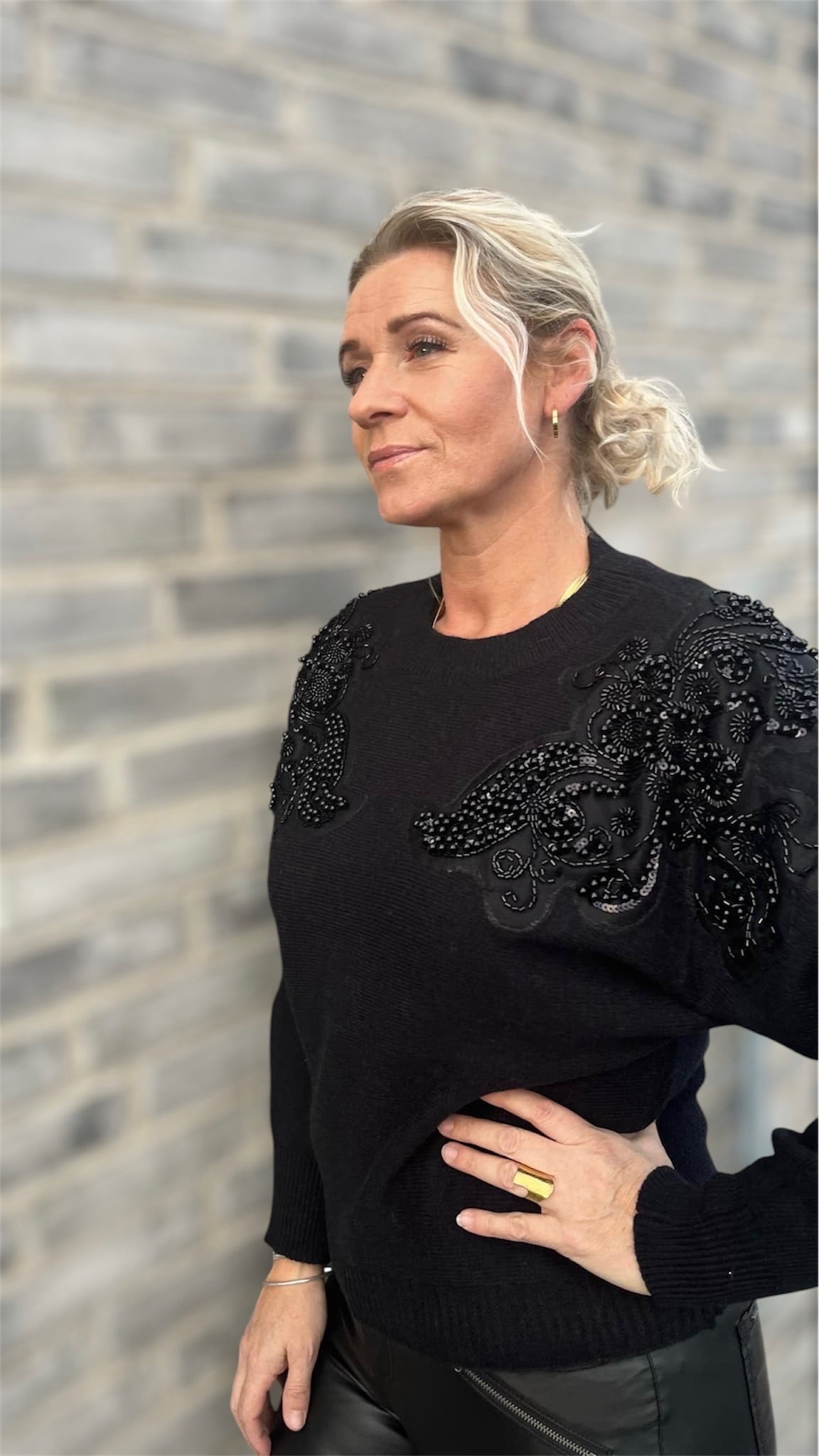 Model iført sort sweater med tone-i-tone paliet- og perledetaljer på skuldrene – en diskret wow-effekt til hverdagens outfit.