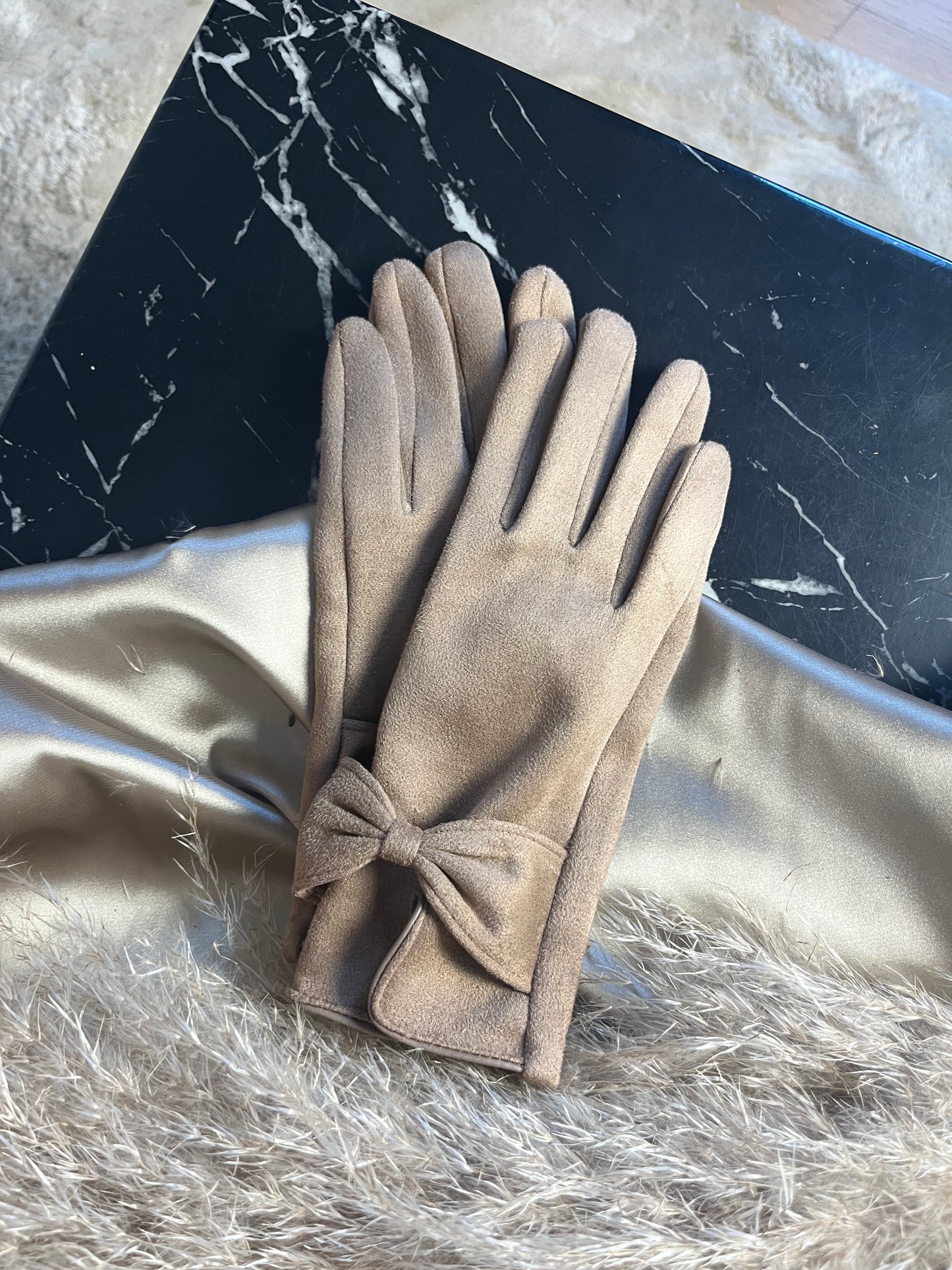 Nærbillede af den feminine sløjfedetalje på de beige suede handsker fra Spohr Copenhagen – en lille detalje med stor effekt."​

