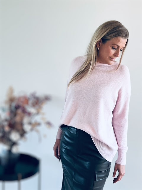 Kvinde iført lyserød strik og sort skindnederdel – elegant og afslappet look med feminine detaljer