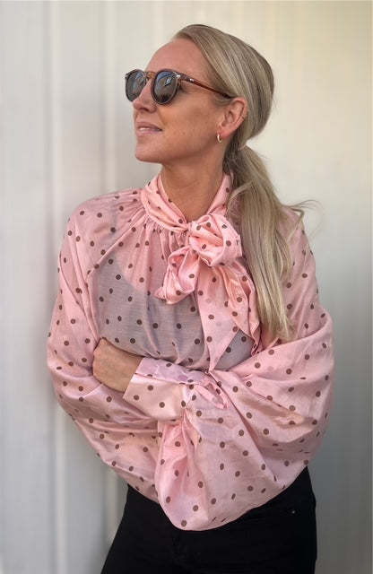 Kvinde i rosa prikbluse med stor sløjfe – et feminint og legende look i sollys