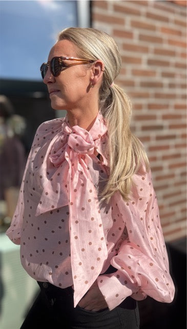 Portræt af kvinde i rosa prikmønstret bluse med dramatisk sløjfe – moderne vintage vibes

